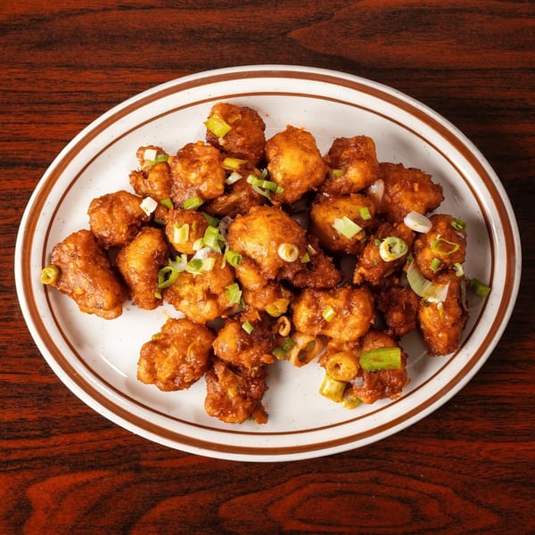 A white oval plate with a brown rim filled with crispy fried cauliflower florets garnished with green onions.