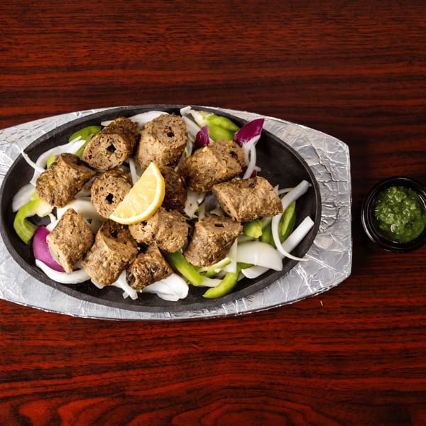 Sizzling platter of seekh kebabs with sliced onions, green peppers, and a lemon wedge.