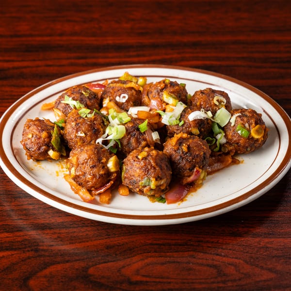 A plate of Manchurian vegetable balls with chopped scallions and onions on a wooden table.