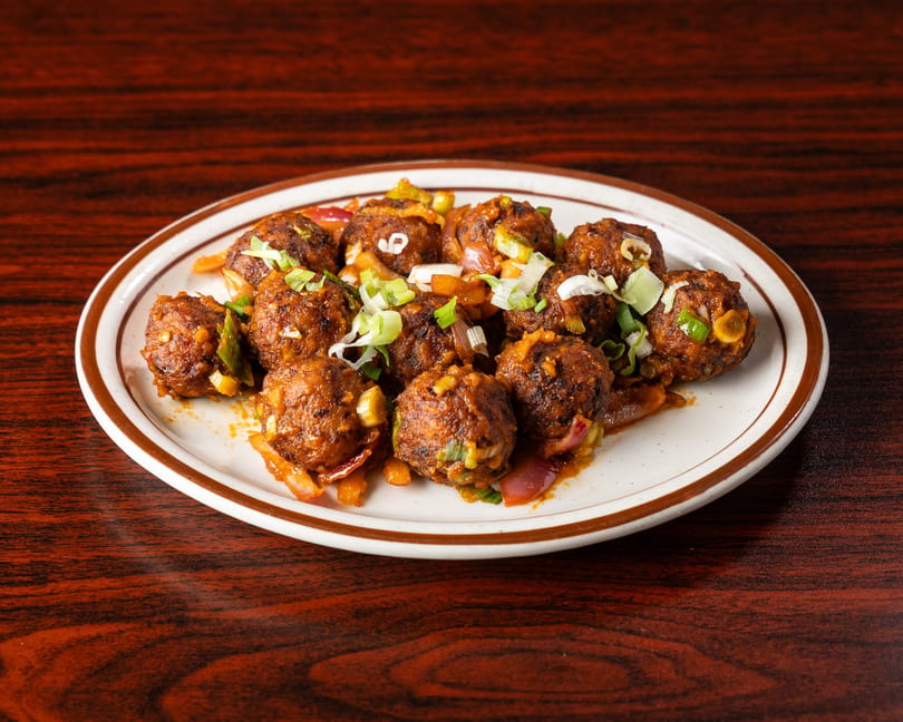 A plate of Manchurian vegetable balls with chopped scallions and onions on a wooden table.