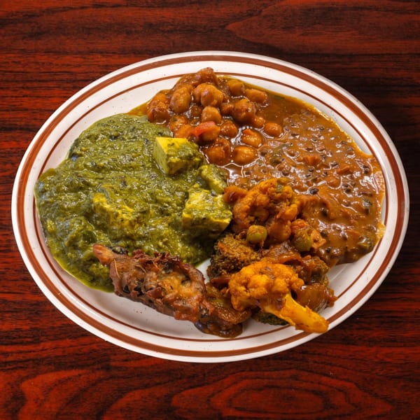 A white plate with brown stripes holds a variety of Indian dishes on a wooden table.