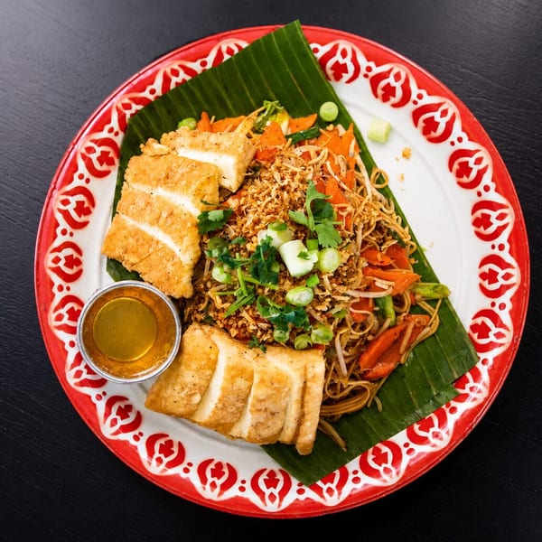 Pad See Ew with crispy tofu, garnished with cilantro and scallions, served on a banana leaf.