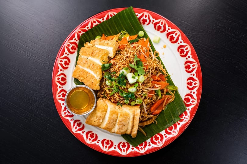 Pad See Ew with crispy tofu, garnished with cilantro and scallions, served on a banana leaf.