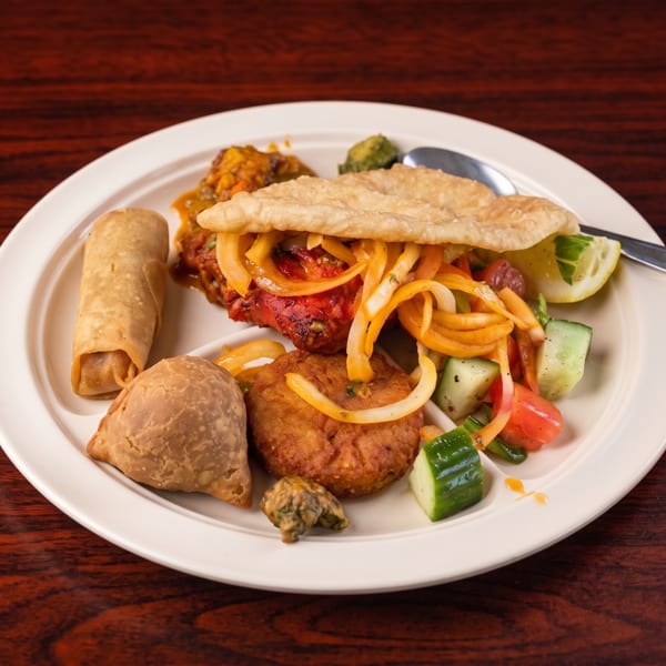 A white plate filled with various Indian dishes, including samosas, pakoras, and a flatbread.