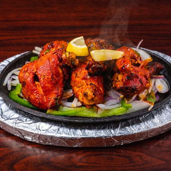 Steaming tandoori chicken with lemon, onions, and green peppers on a sizzling platter.