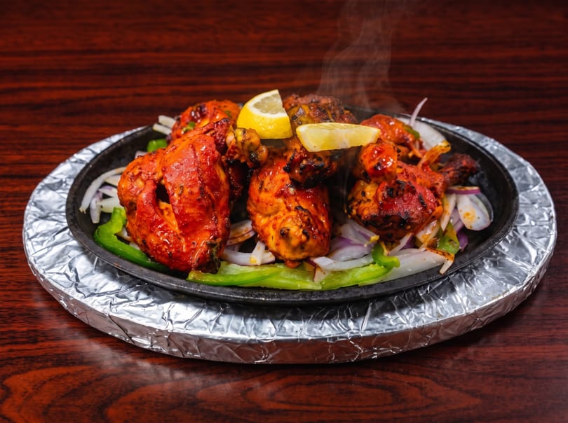 Steaming tandoori chicken with lemon, onions, and green peppers on a sizzling platter.