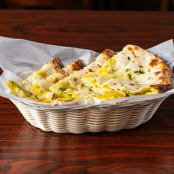 A white basket filled with pieces of golden-brown naan bread, some with yellow filling, on a wooden table.
