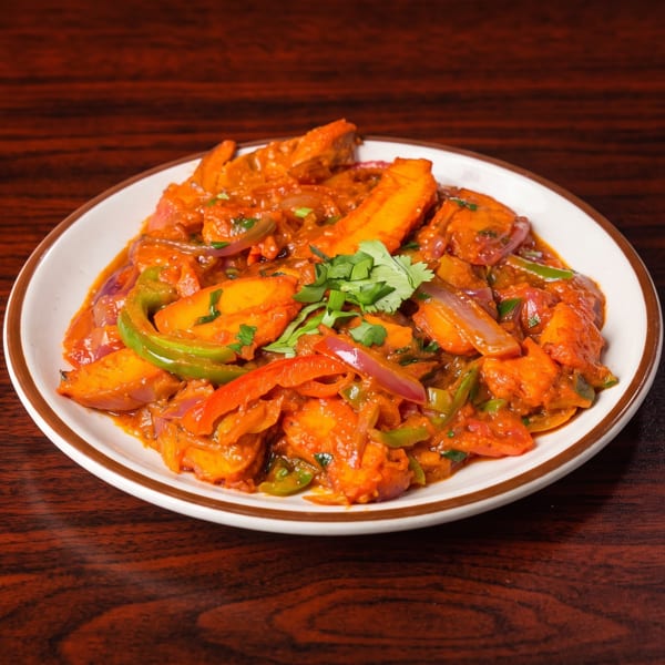 A plate of chili paneer, with red and green peppers, onions, and cilantro, on a wooden table.