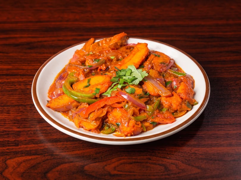 A plate of chili paneer, with red and green peppers, onions, and cilantro, on a wooden table.