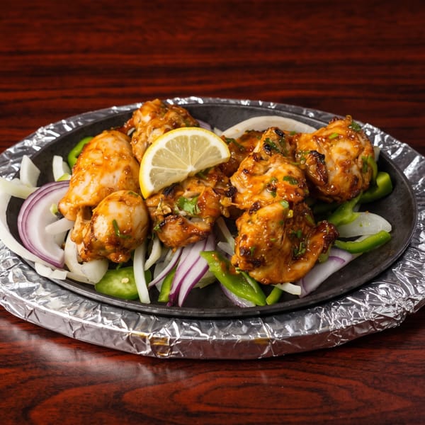Sizzling chicken tikka with onions, green peppers, and a lemon slice on a foil-wrapped platter.