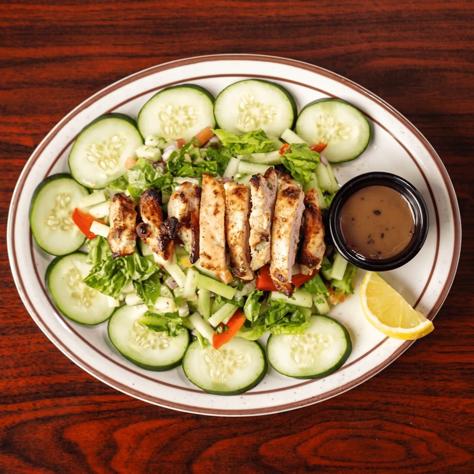 Grilled chicken salad with cucumbers, lettuce, red peppers, and a side of dressing and lemon.