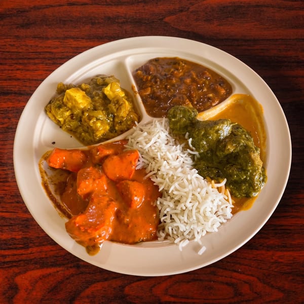 A divided plate of Indian food with rice, paneer, dal, chicken tikka masala, and saag.